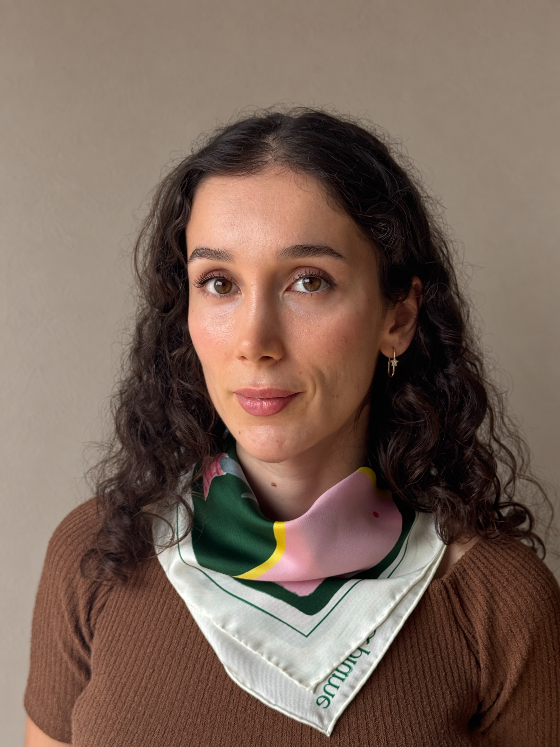 The Italian Greyhound silk scarf worn at the neck with a brown knit, showing its pink, green and ivory folds across the shoulders and chest.